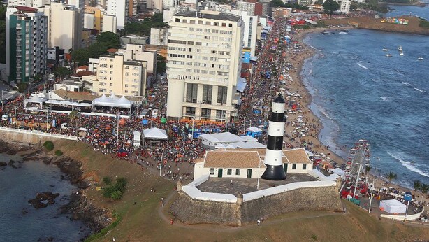 Un paisaje urbano costero con un faro, playa y una zona urbana densa.