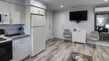 Eine moderne Küche mit weißen Schränken, einem Kühlschrank und einer Mikrowelle. An der Wand ist ein Fernseher angebracht und es gibt eine kleine Sitzecke mit zwei Stühlen.
