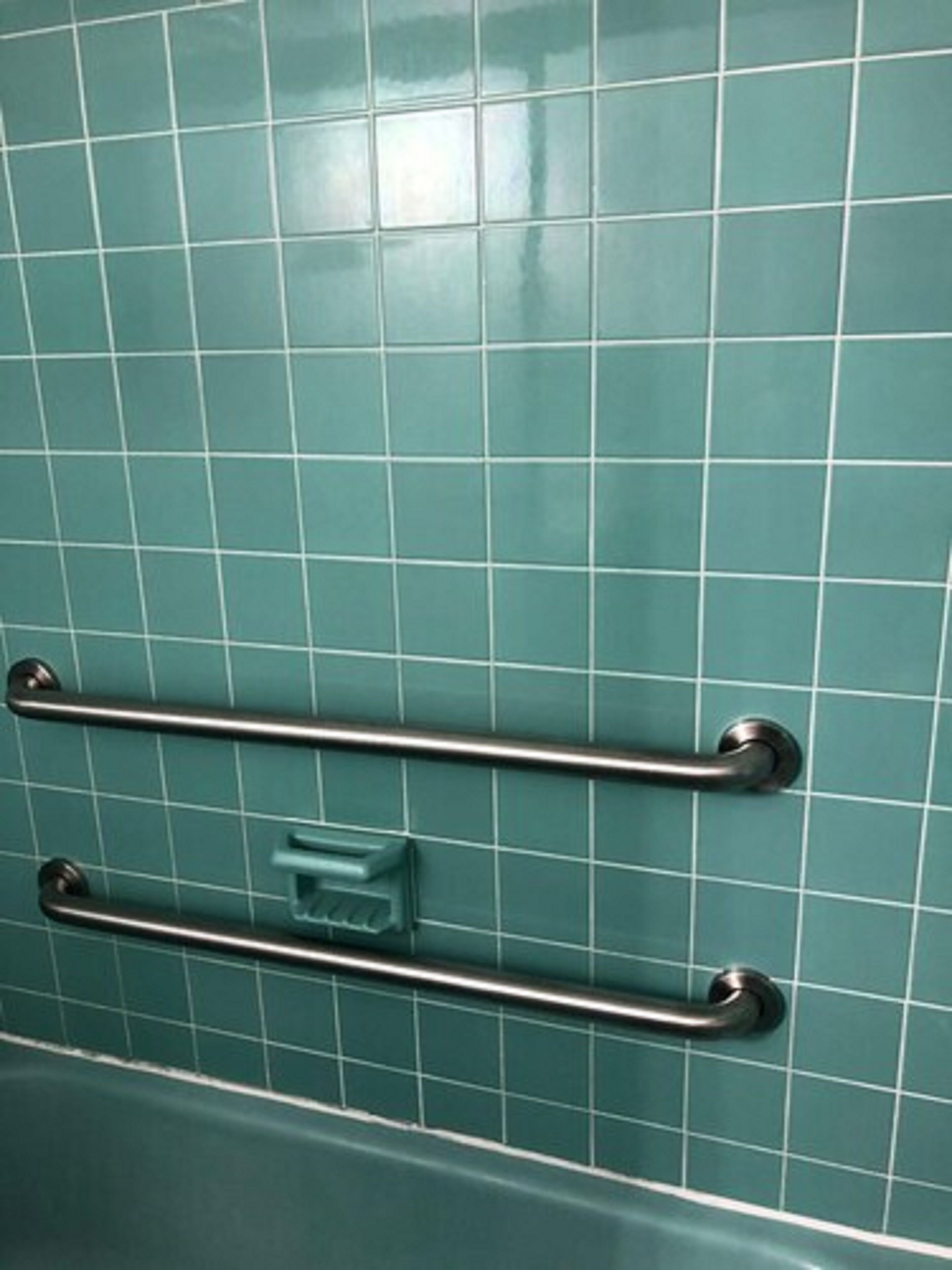Une salle de bain avec des carreaux de couleur turquoise et une barre d’appui fixée au mur.