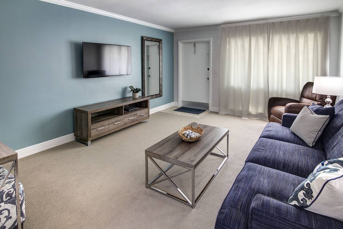 A living room with a blue sofa, a wooden coffee table, a TV, and a mirror.