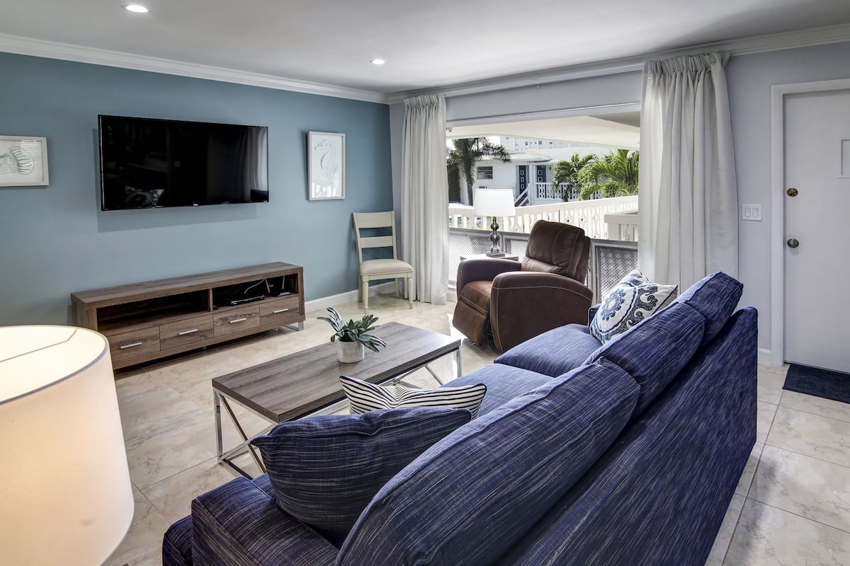 A living room with a sofa, TV, and a balcony with curtains.