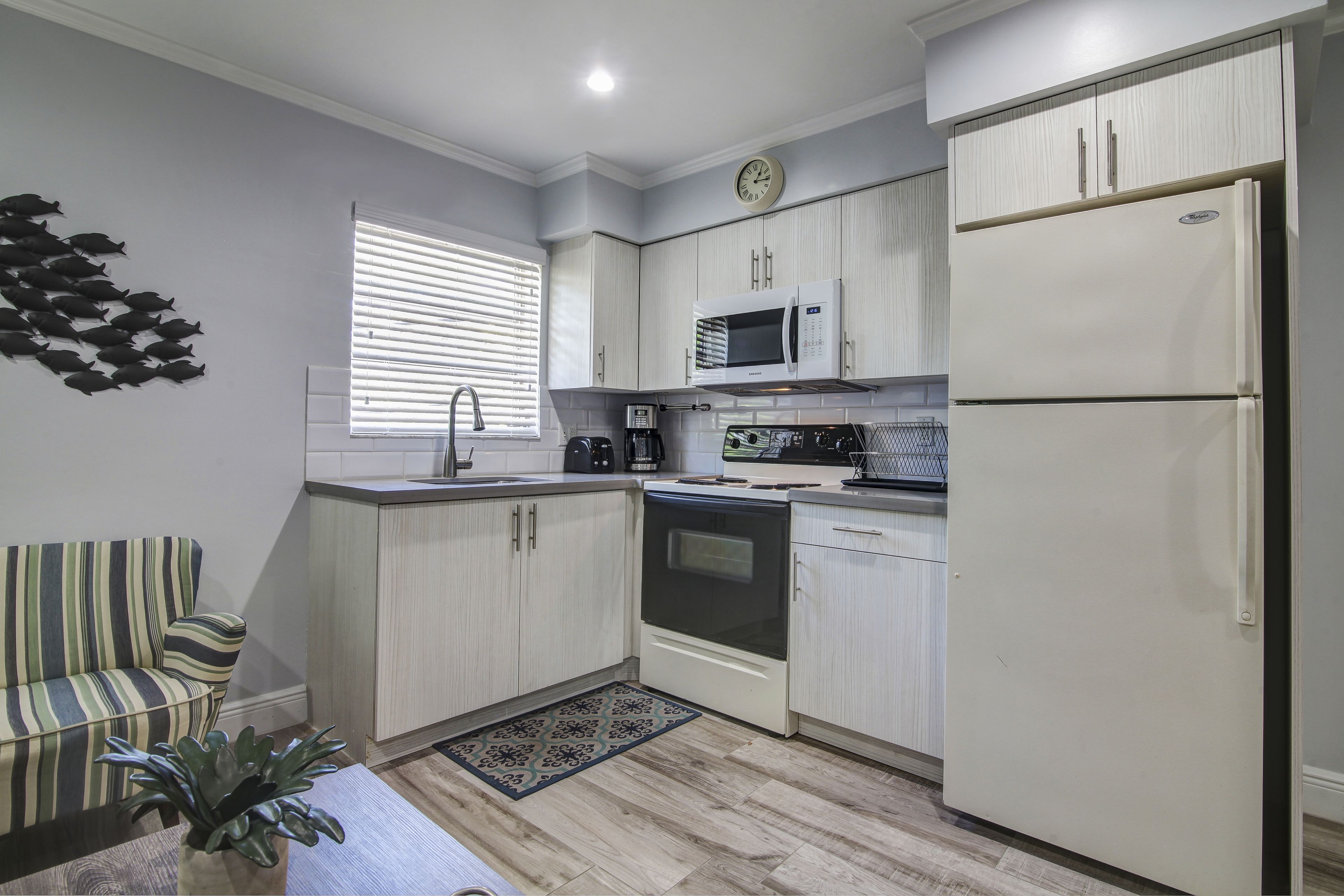 A compact kitchen with white cabinets, a microwave, a refrigerator, and a stove.
