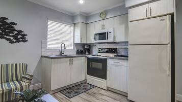 A compact kitchen with white cabinets, a microwave, a refrigerator, and a stove.