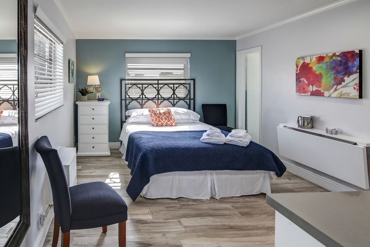 A neatly arranged bedroom with a bed, bedside table, lamp, and a colorful artwork on the wall.