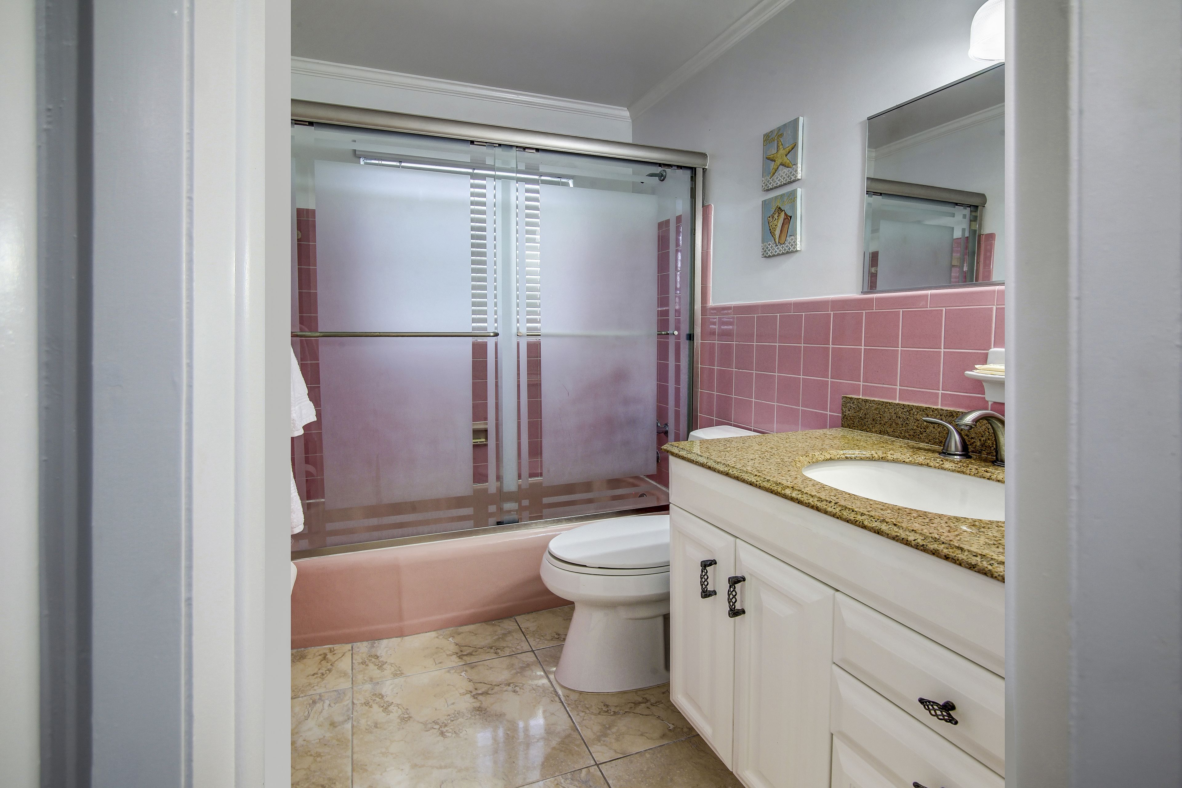 A bathroom with a glass-enclosed shower, a white toilet, a sink with a granite countertop, and pink-tiled walls.