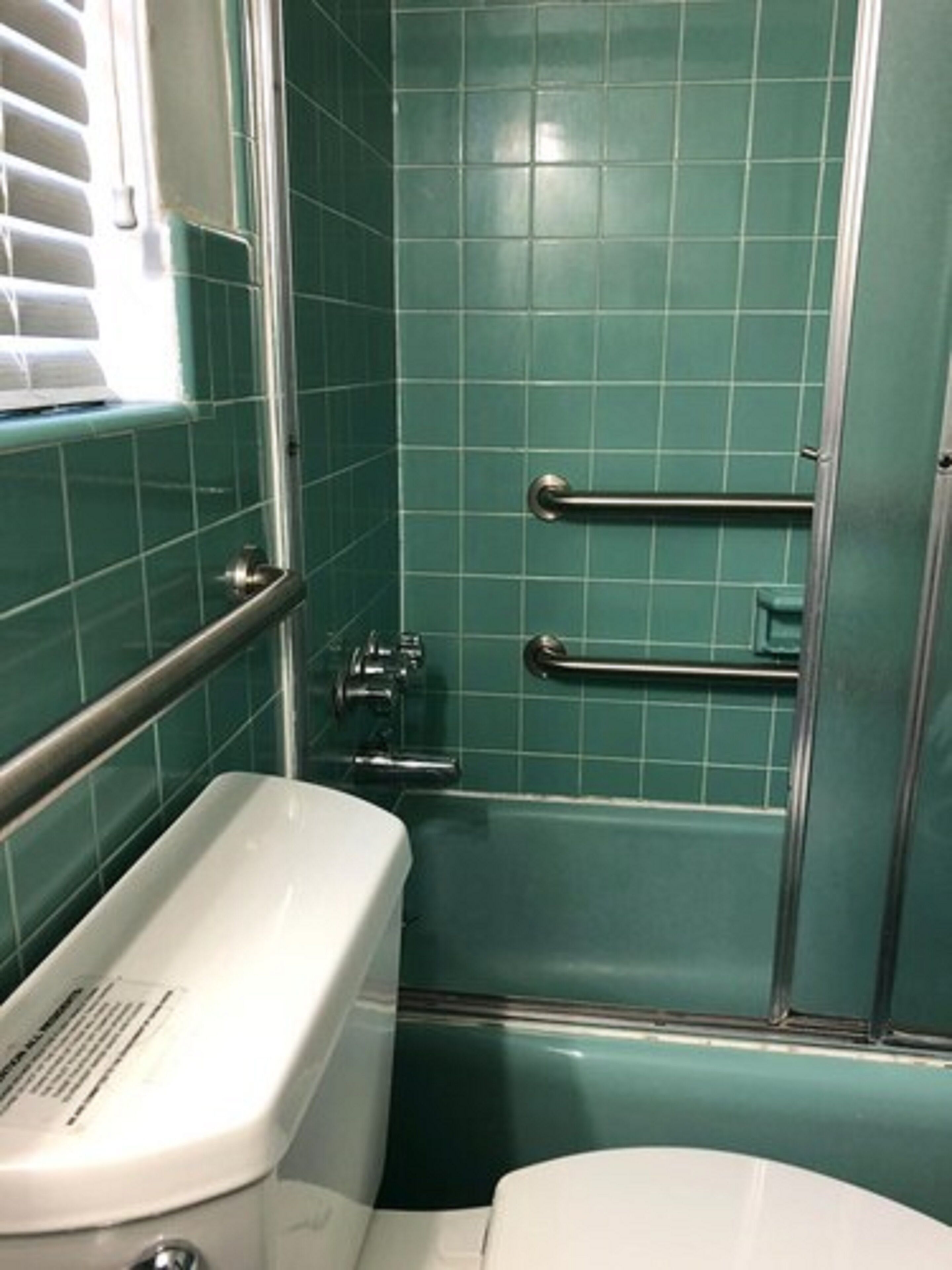 Un bagno con una vasca da bagno bianca, un water bianco e una doccia con porta in vetro. Sono presenti due maniglie metalliche per la sicurezza.