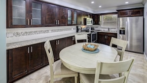 A modern kitchen with dark wooden cabinets, a white dining table, and a stainless steel refrigerator.