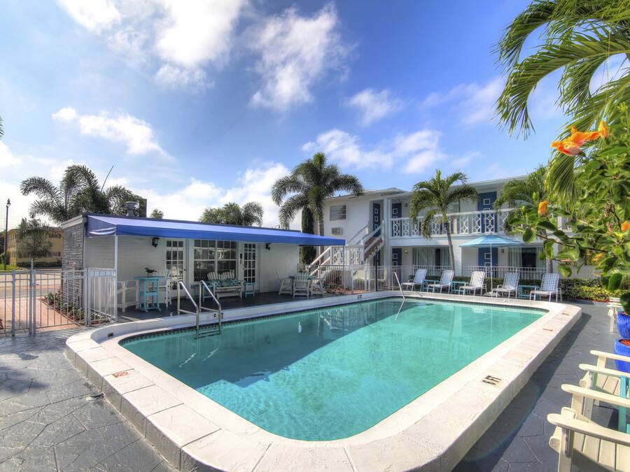A swimming pool with a blue canopy, white lounge chairs, and a building with a balcony in the background.