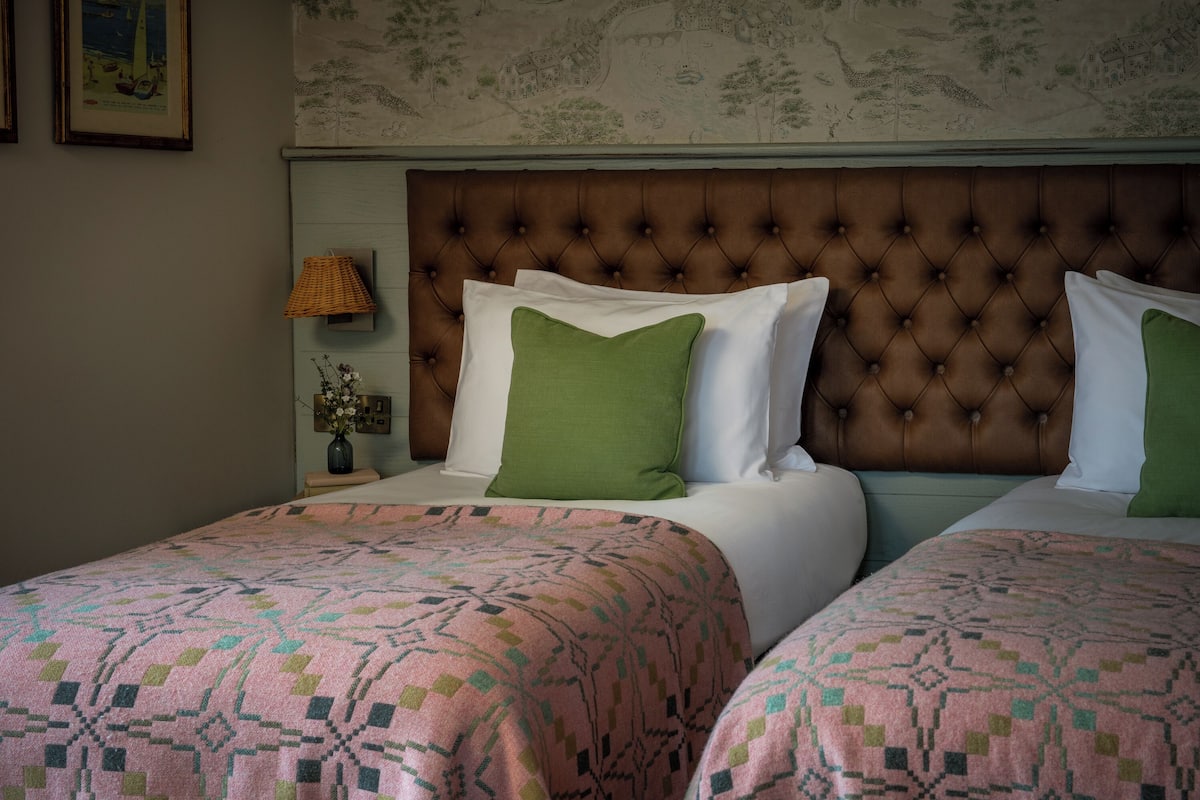Habitación de hotel con dos camas, un cabecero con capitoné, una mesita de noche con lámpara y una pared con un mural de un mapa.
