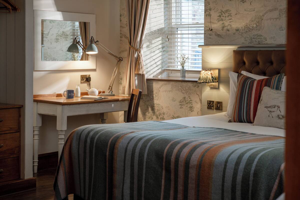 Un dormitorio con cama, mesita de noche, lámpara y ventana con cortinas.