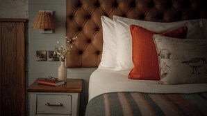 Ein Schlafzimmer mit einer gesteppten Kopfteil, einem Nachttisch mit Lampe, einer Vase mit Blumen und einem Bett mit gestreifter Bettwäsche.