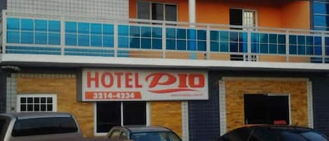 A two-story building with a sign for 'HOTEL PIO' and a contact number. There are three cars parked in front.