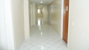 A long, narrow hallway with white tiled floors and beige walls. - Hotel Pio (Teresina)