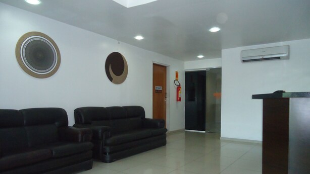 A reception area with two black sofas, a wooden door, a fire extinguisher, and a modern air conditioning unit on the wall. - Hotel Pio (Teresina)