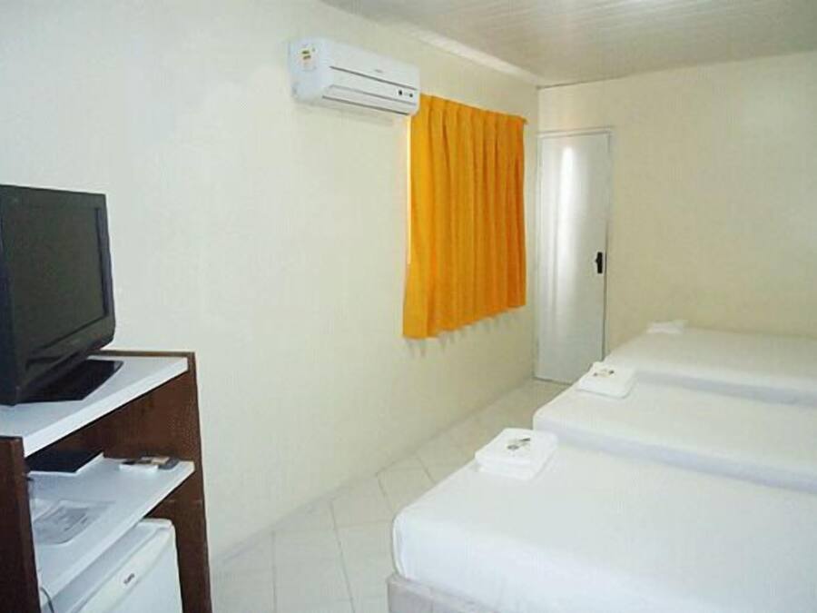 Una habitación de hotel con una televisión sobre un escritorio, una cama con colchón blanco, un equipo de aire acondicionado y un armario.