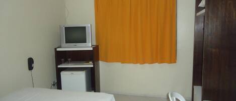 A small, simple room with a bed, a desk with a computer, a television, and a wardrobe.