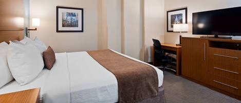 A hotel room with a bed, a desk, a television, and two framed pictures on the wall.