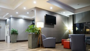 A modern lobby with a flat-screen TV mounted on the wall, a large potted plant, and a seating area with a red ottoman. - Best Western Plus Philadelphia Convention Center Hotel (Philadelphia)