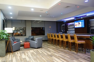 Un área de bar moderna con televisión, asientos y piso de madera.