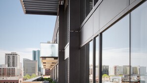 A modern balcony with a wooden bench, a glass railing, and a view of the cityscape. - The Maven Hotel at Dairy Block (Denver)