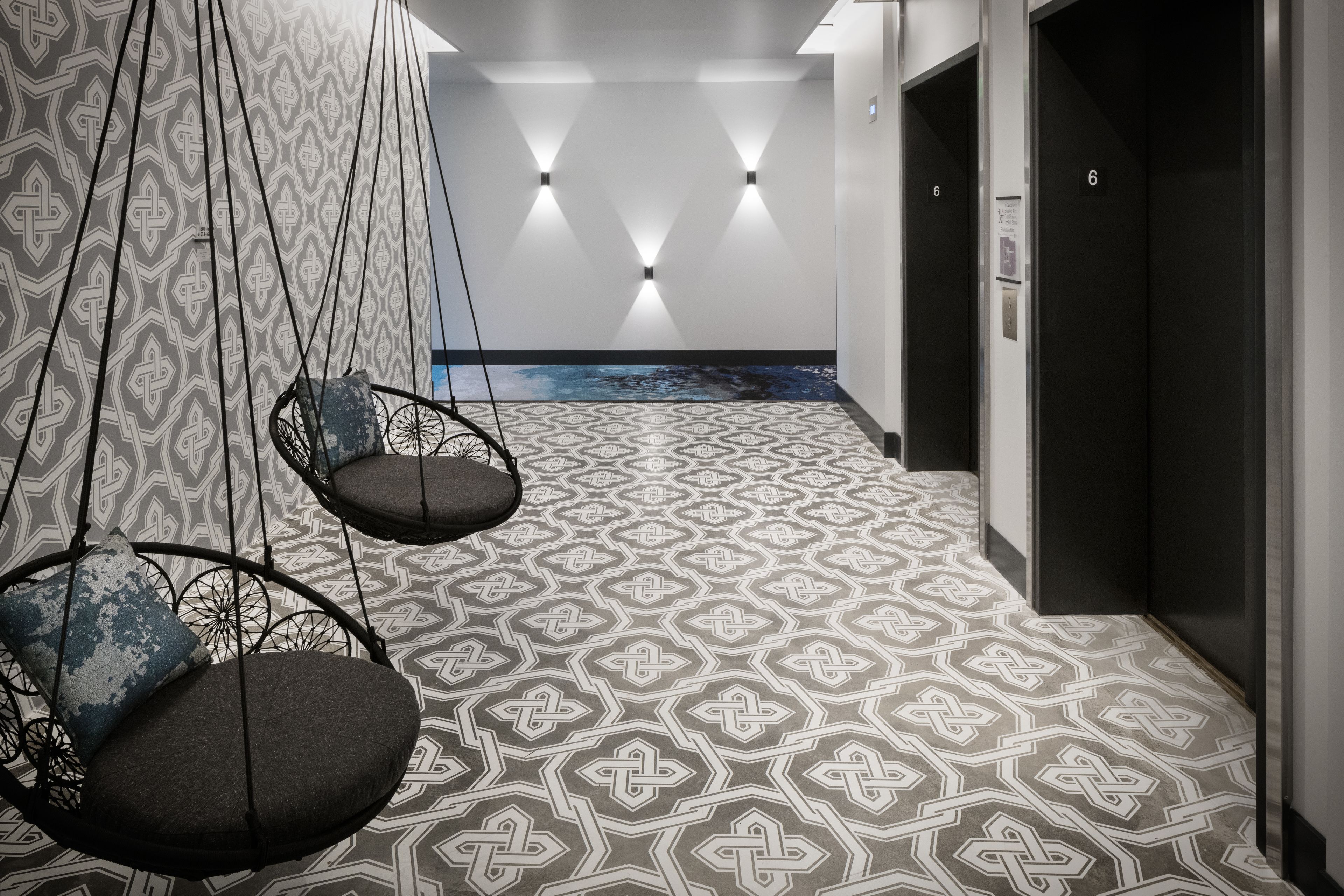 A modern hallway with geometric patterned flooring, hanging chairs with cushions, and wall-mounted lighting.