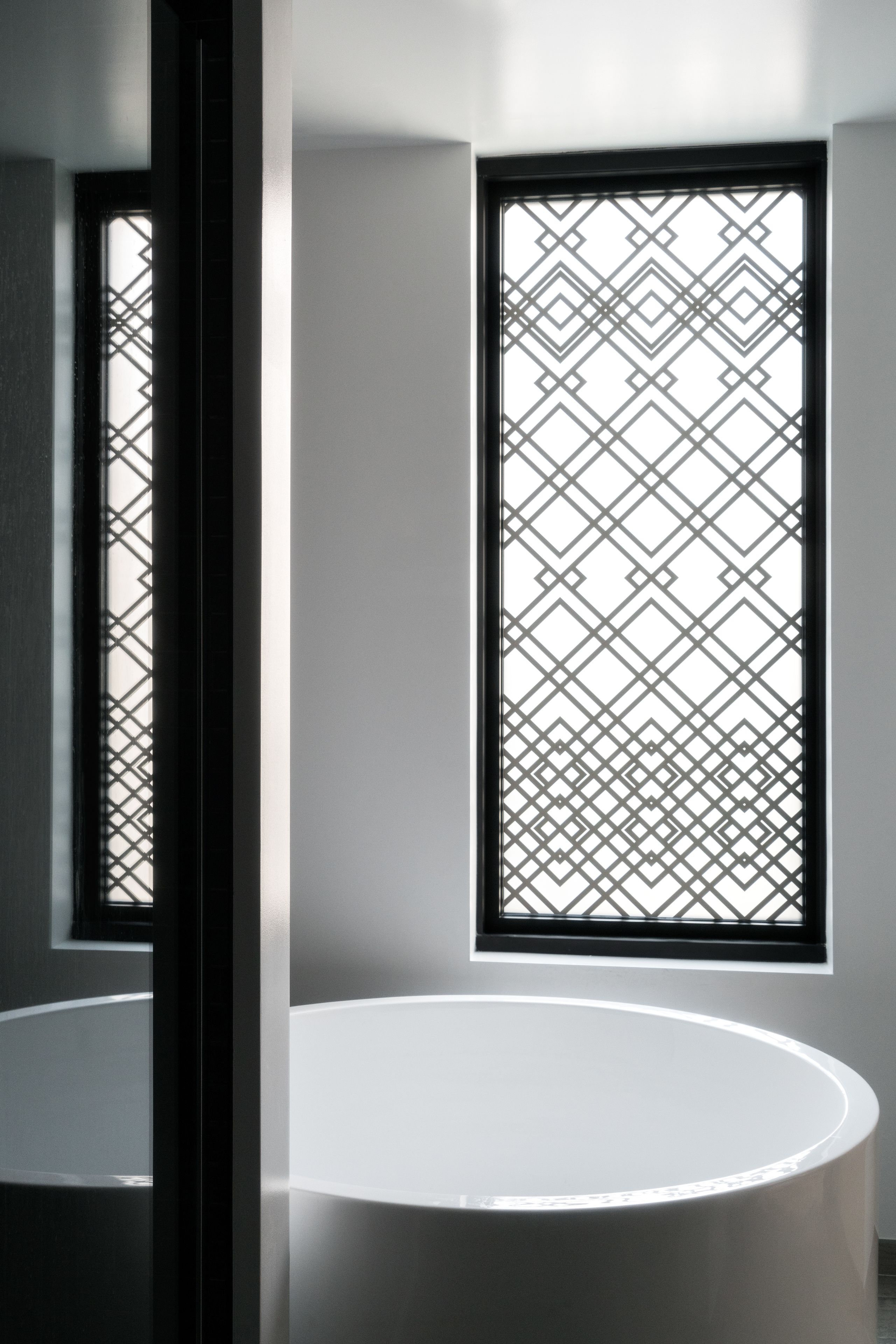 A room with a round white table, a window with a geometric pattern, and a door frame.