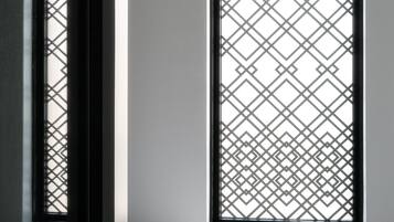 A room with a round white table, a window with a geometric pattern, and a door frame.