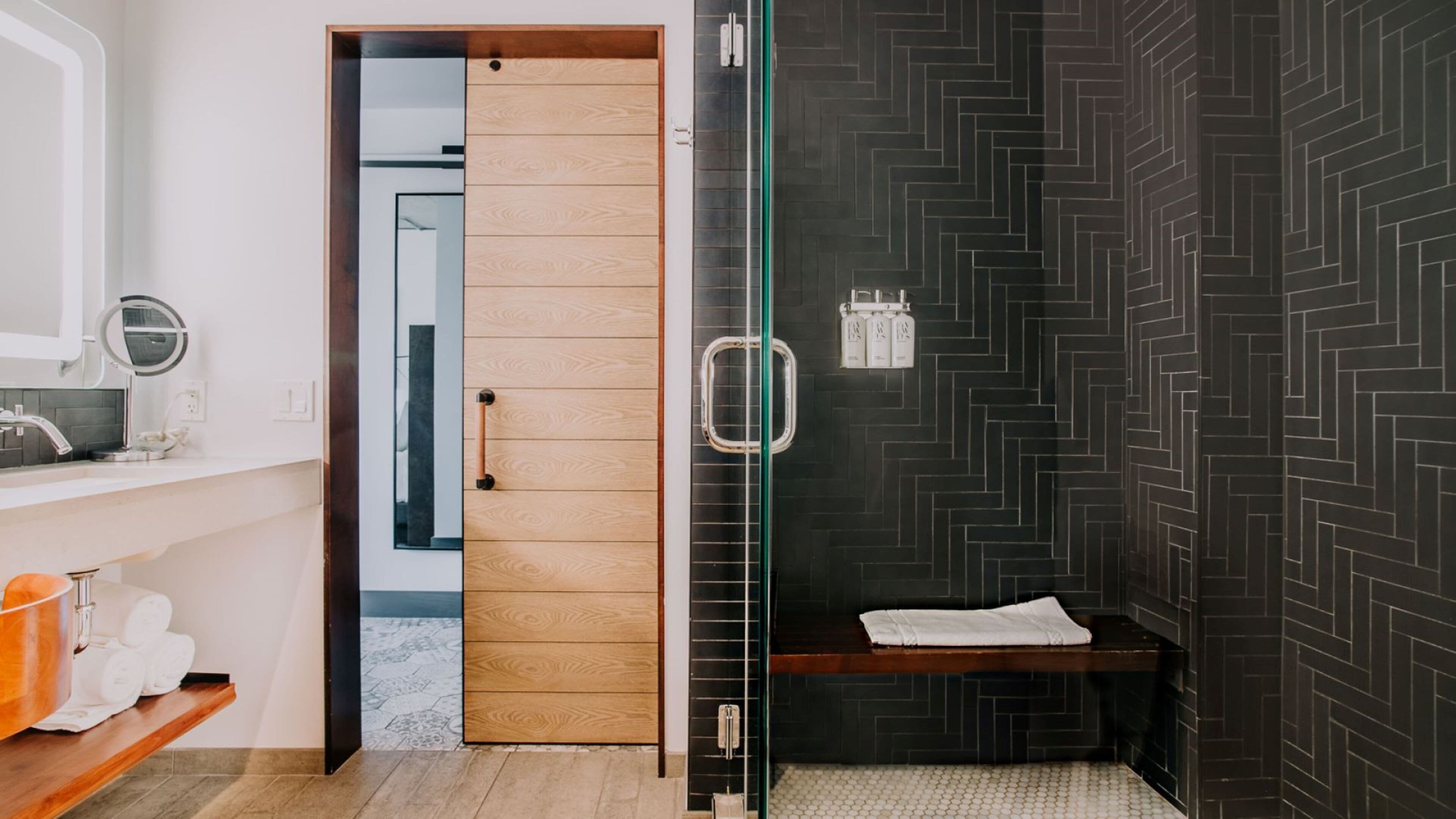 A modern bathroom with a wooden door, a glass shower enclosure, and a black tiled wall.