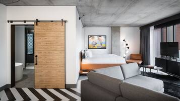 Habitación de hotel moderna con cama, sofá, televisor y puerta corredera que da al baño.