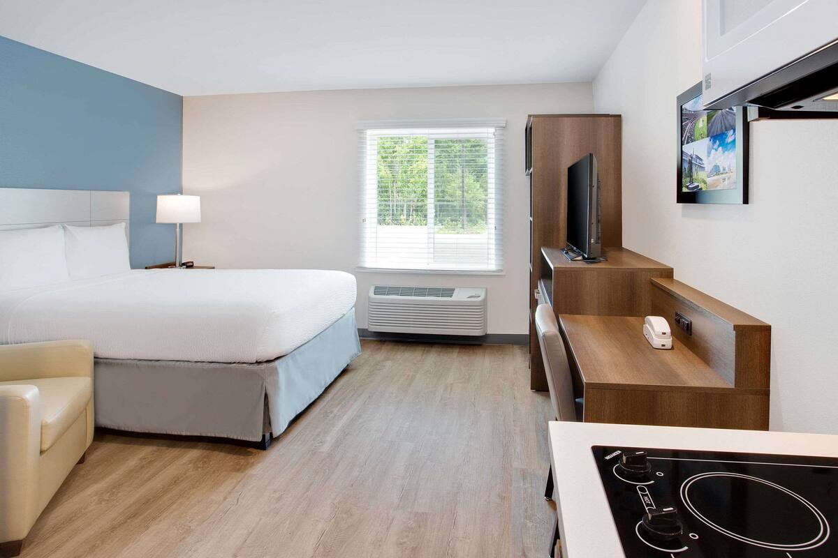 A hotel room with a bed, a desk, a TV, and a window with blinds.