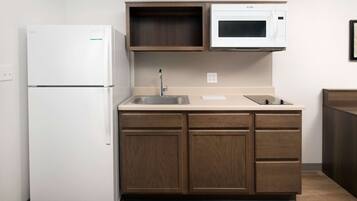 A compact kitchen with a white refrigerator, a microwave, a sink, and wooden cabinets.