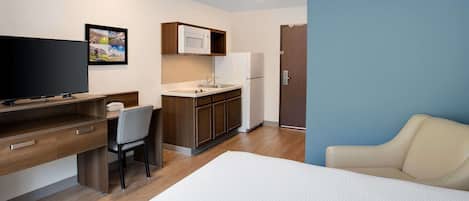 Habitación de hotel con cama, escritorio con silla, kitchenette y puerta.