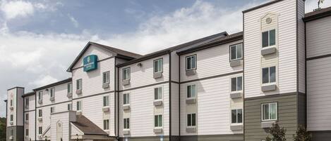 A multi-story hotel with a flat roof, large windows, and a parking lot in front.
