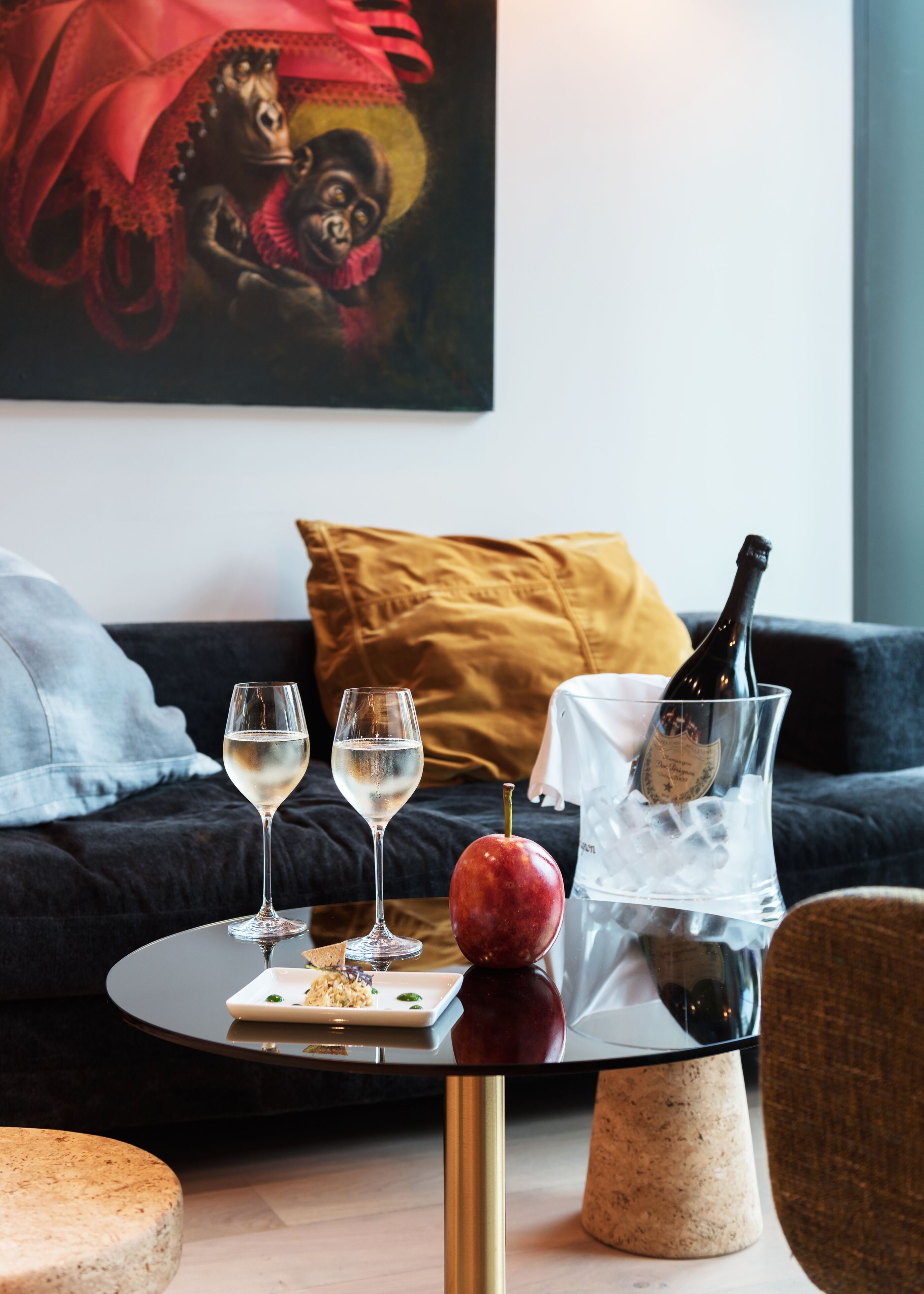 Un salon moderne avec une table ronde en verre, deux verres à vin, une bouteille de champagne et une pomme posée sur la table.