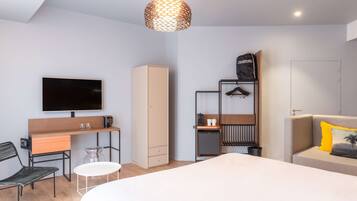 Una habitación de hotel moderna con cama, escritorio, televisión, armario y zona de estar.
