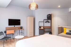 Una habitación de hotel moderna con cama, escritorio, televisión, armario y zona de estar.