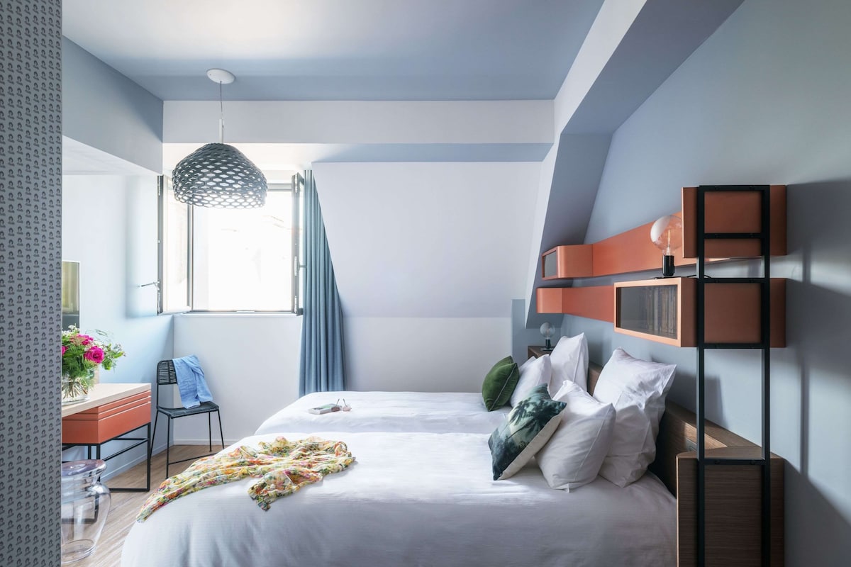 Un dormitorio moderno con una cama grande, un escritorio con silla, una lámpara colgante y una ventana con cortinas.