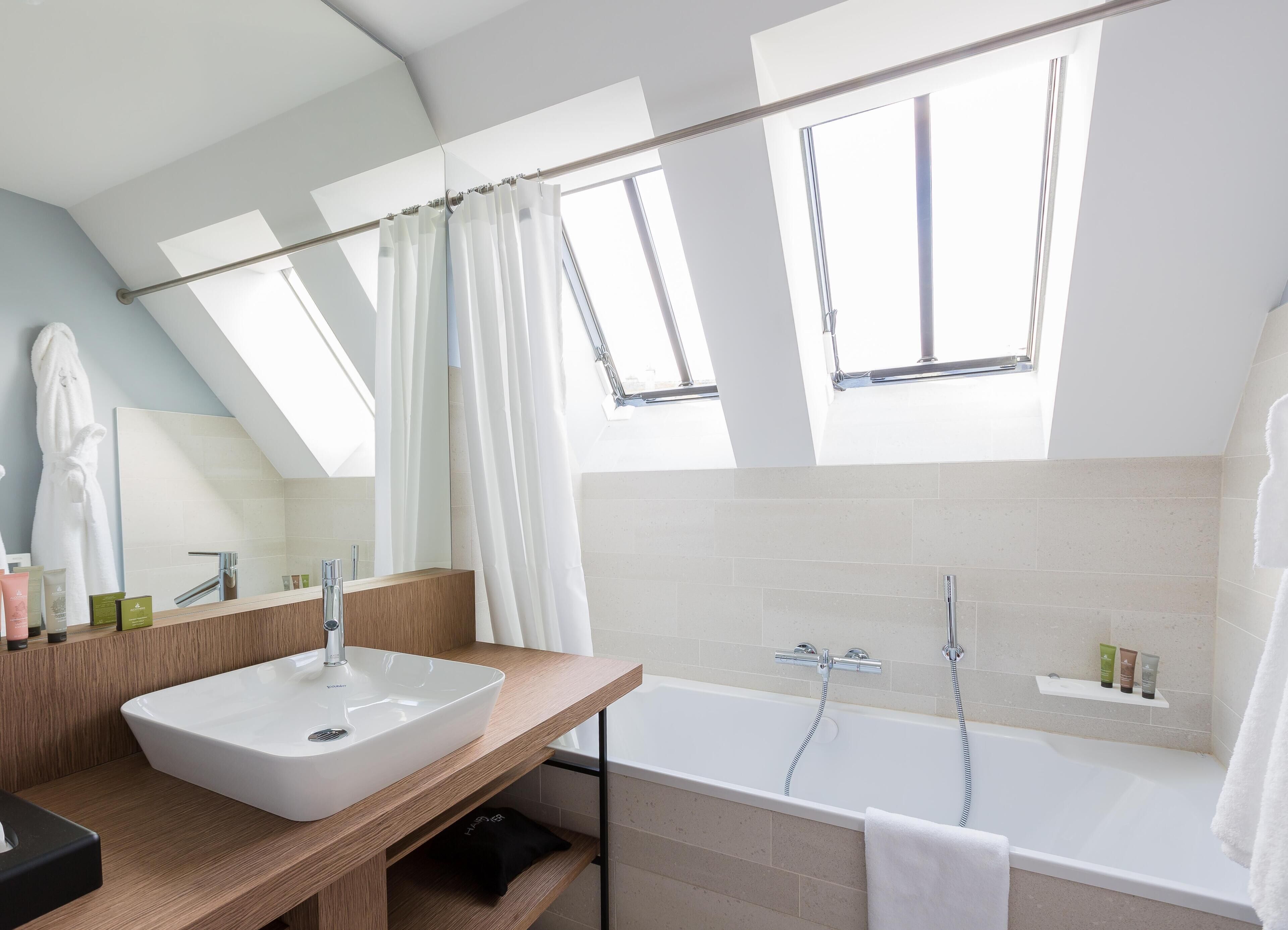 Un baño moderno con tragaluz, bañera, tocador con lavamanos y un perchero para toallas.