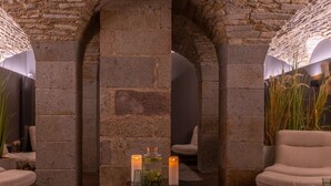 A room with stone walls, a central archway, a small table with candles, and a sofa. - Golden Tulip Saint Malo - Le Grand Bé (Saint-Malo)