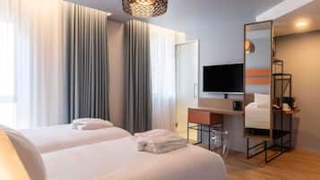 A hotel room with two beds, a TV, a mirror, and a large window with curtains.