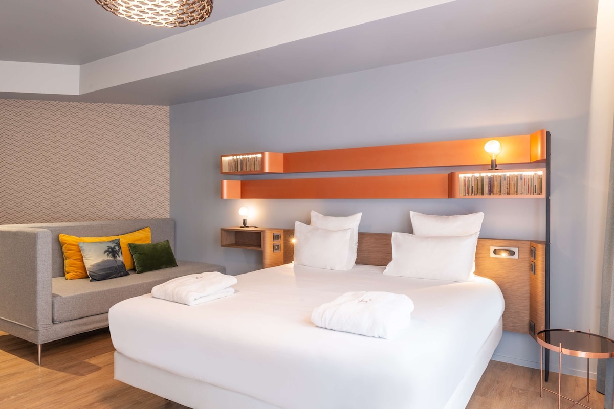 Una habitación de hotel moderna con una cama grande, un sofá y una lámpara de lectura.