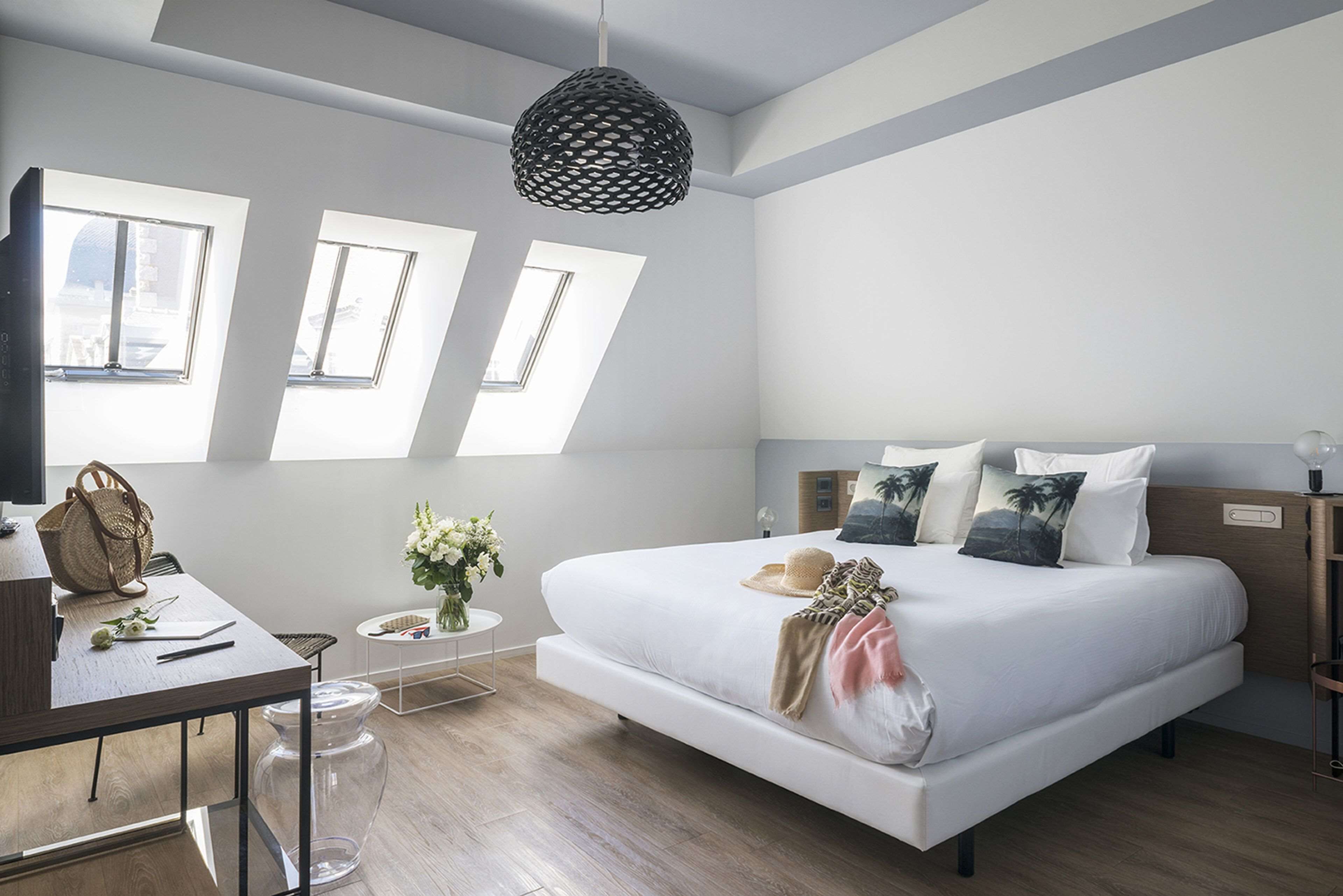 A modern bedroom with a large bed, skylights, a desk, and a hanging light fixture.