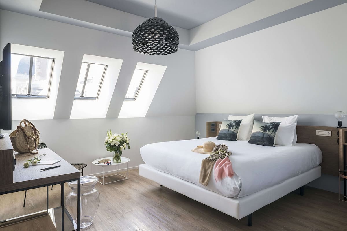 Ein modernes Schlafzimmer mit einem großen Bett, Oberlichtern, einem Schreibtisch und einer Pendelleuchte.