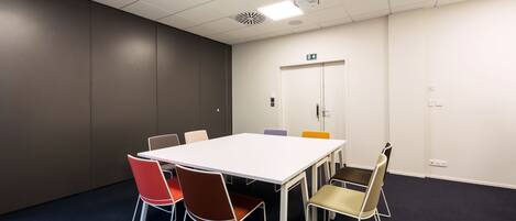 Una sala de conferencias con una mesa blanca, seis sillas y una puerta con letrero de salida de emergencia.