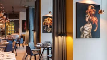 Uma sala de jantar moderna com mesas preparadas para refeição, um bar ao fundo e obras de arte nas paredes.