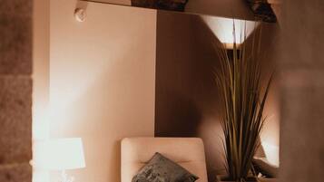 Ein gemütliches Zimmer mit einem gepolsterten Sessel, einem kleinen Tisch mit Lampe und einer hohen Pflanze.