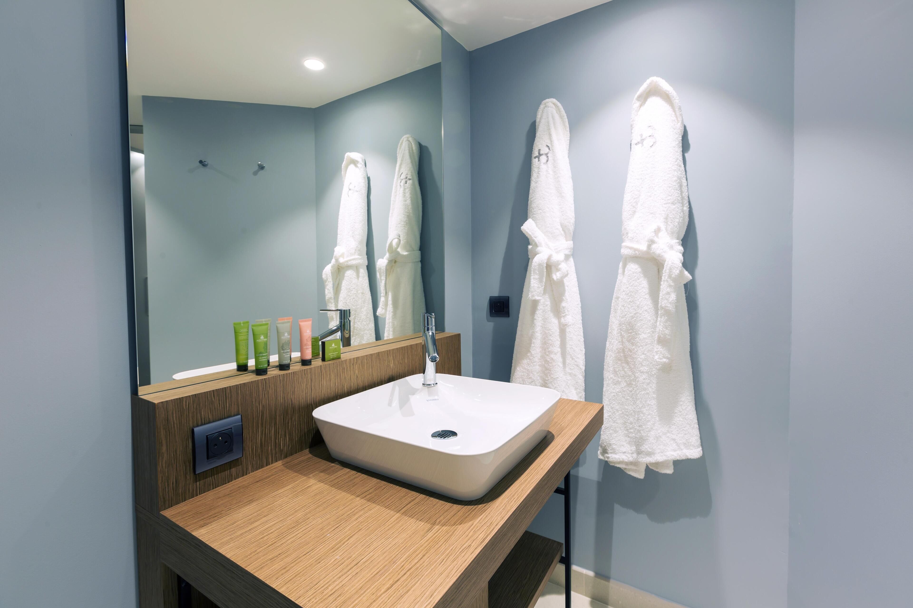 A modern bathroom with a large mirror, white sink, and two white towels hanging on the wall.