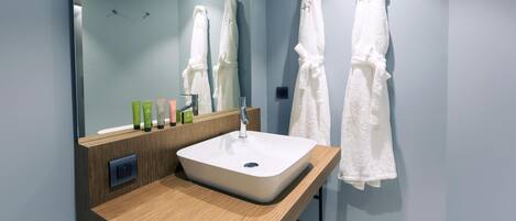 A modern bathroom with a large mirror, white sink, and two white towels hanging on the wall.