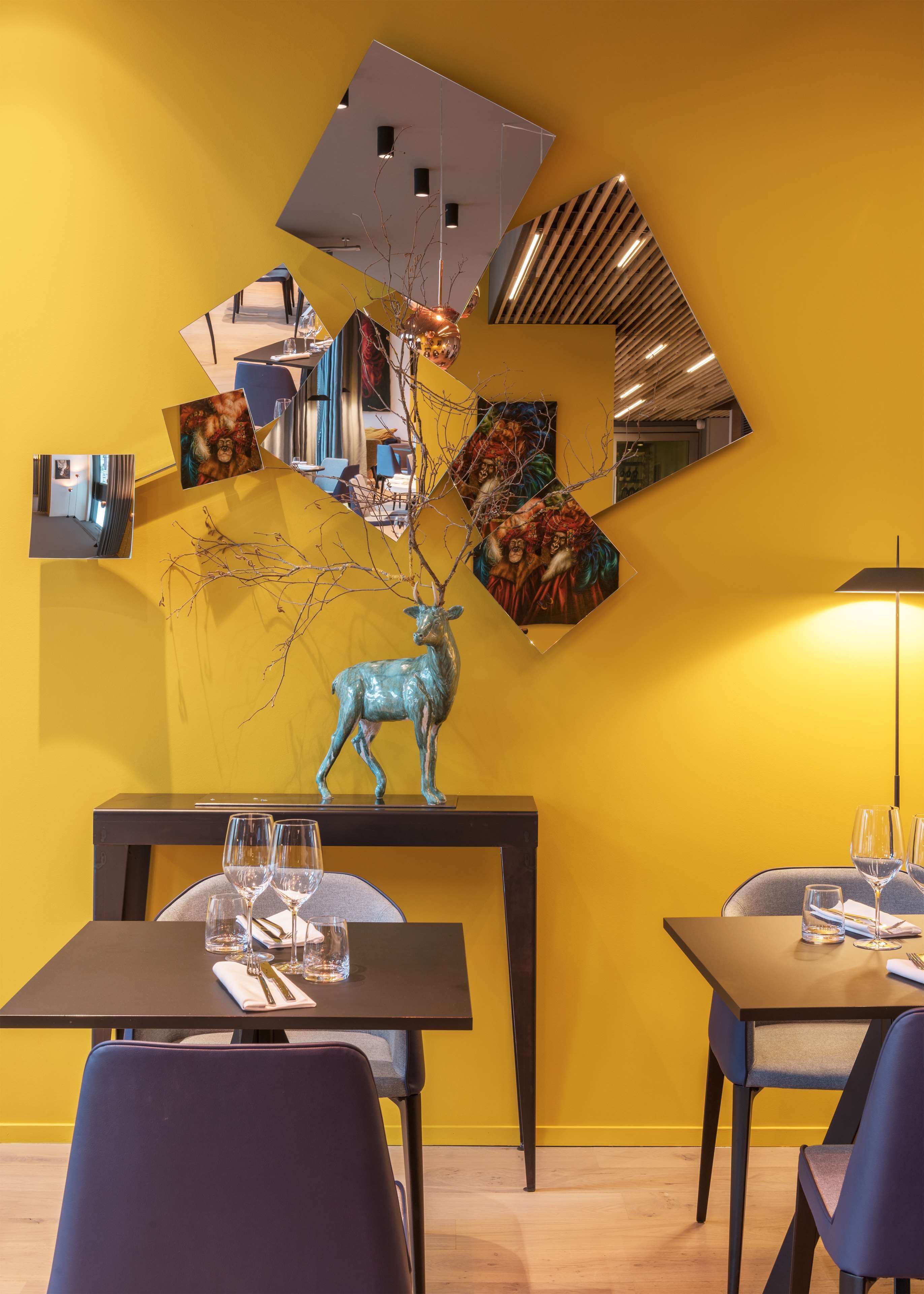 Un comedor con pared amarilla, una mesa dispuesta con vasos y cubiertos, y una escultura decorativa de un ciervo.