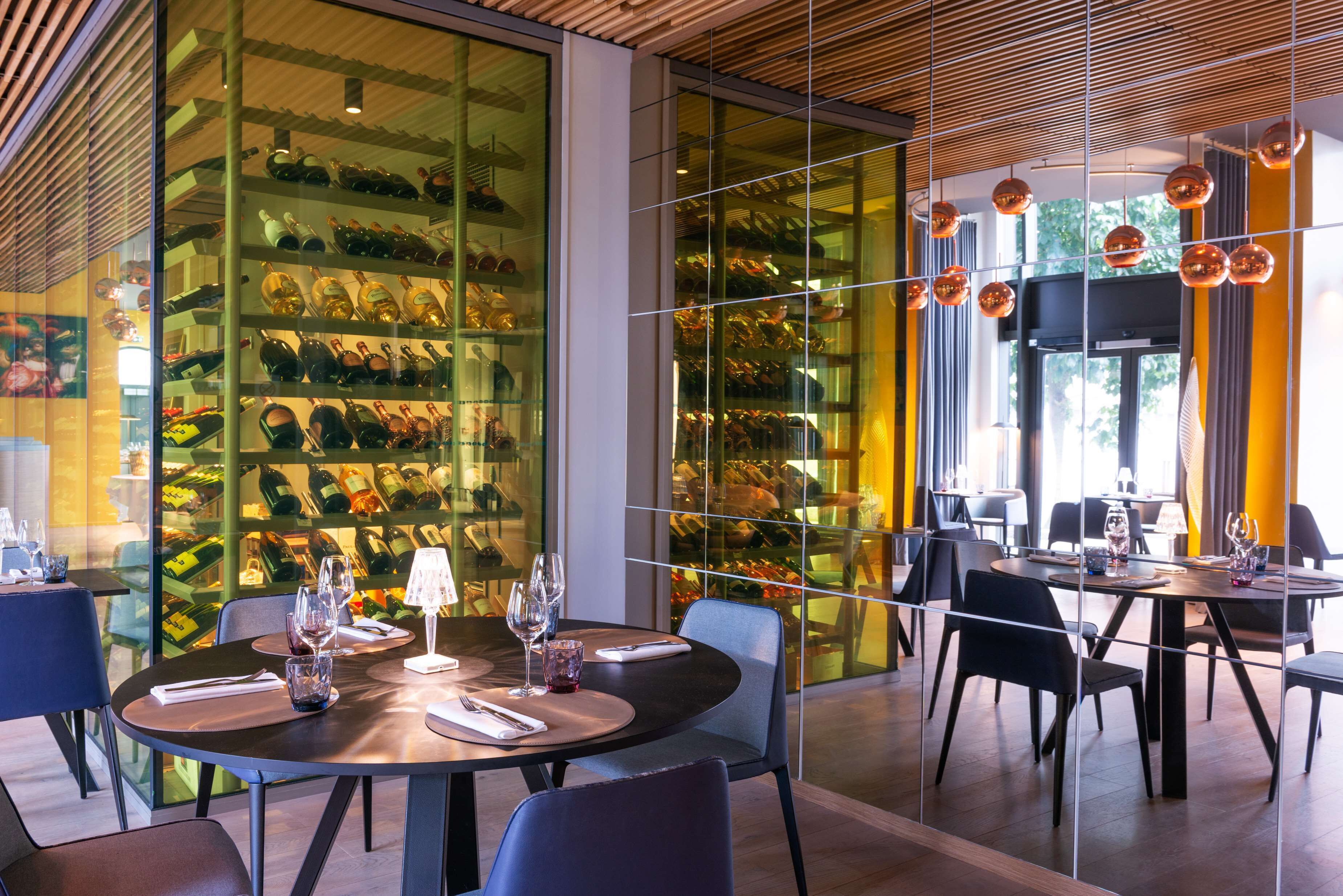 A restaurant with round tables, chairs, and a wine rack filled with bottles.